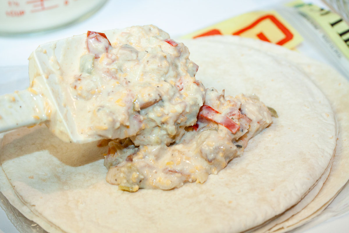 Large spatula full of creamy white enchilada filling peing placed on the center of a flour tortilla