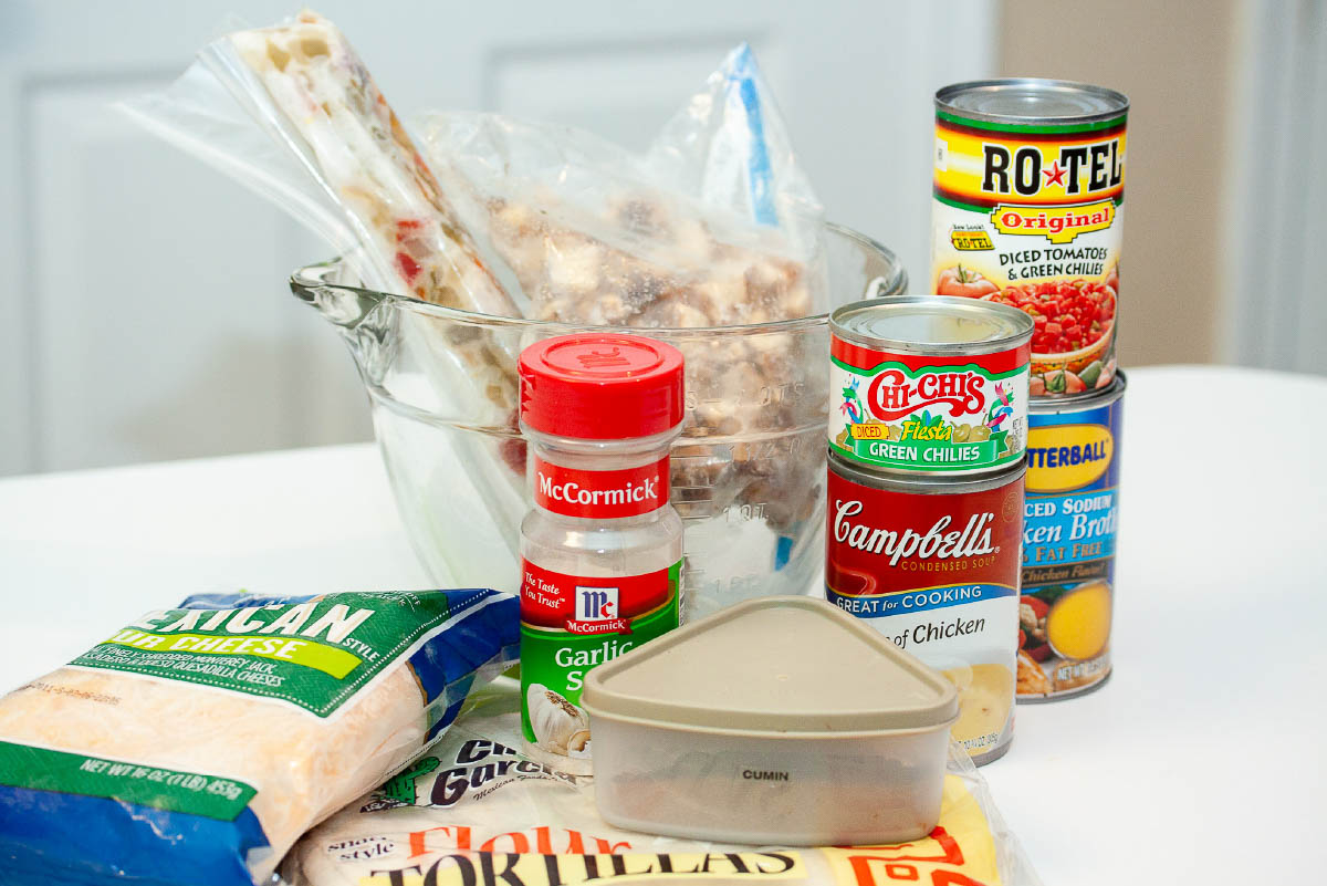 Ingredients for creamy chicken enchiladas: cooked chicken, cooked onion & bell peppers, cumin, garlic salt, green chilis, Rotel tomatoes and green chilis, chicken broth, shredded Mexican cheese, and flour tortillas