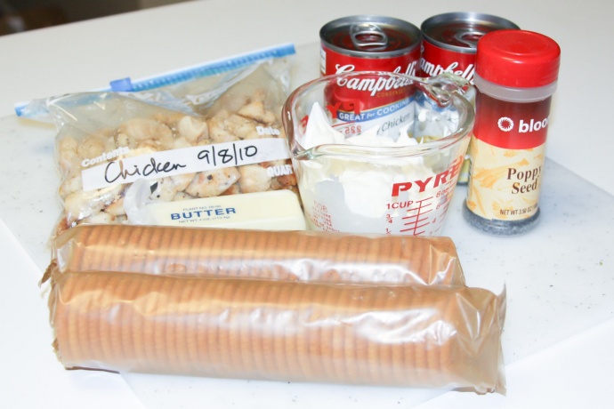 cooked chicken, sour cream in a measuring cup, a stick of butter, 2 sleeves crackers, cream of chicken soup, a jar of poppy seeds