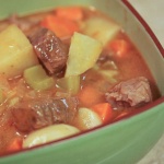 Green bowl with cooked beef cubes, potatoes, carrots, and celery in a tomato-based sauce