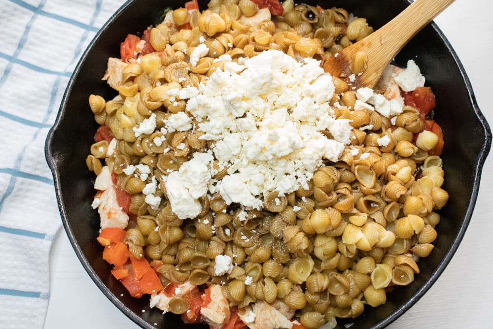 Cast iron skillet with shell pasta, tomatoes, onions, feta cheese, and balsamic vinegar