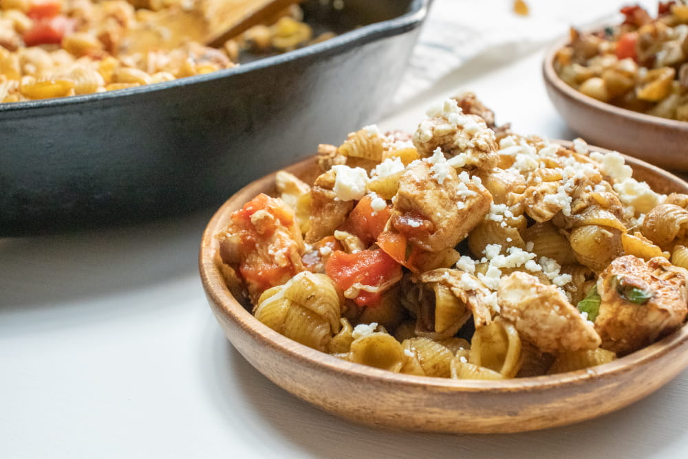 Bowl of shell pasta with tomatoes, feta cheese, and balsamic vinegar with text Mediterranean Chicken with Pasta