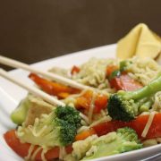 Ramen noodles, broccoli, and bell pepper strips in a bowl with chopsticks.