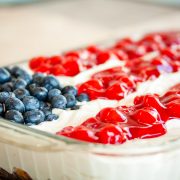 Fluffy white whipped cream mix over crumbled angel food cake topped with blueberies and cherry pie filling in the design of an American flag in a 9x12 glass pan