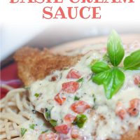 Breaded chicken breast covered with a cream sauce and resting on a plate of spaghetti. Text is Chicken with Basil Cream Sauce - Add Salt & Serve logo