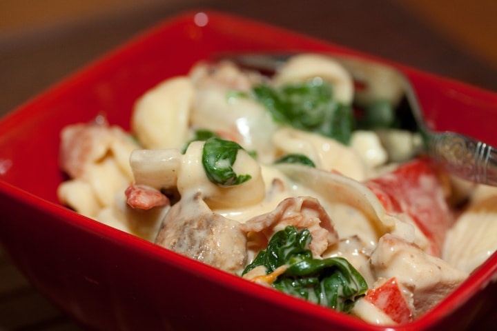 easy-orecchiette-florentine-feat-min Red square bowl with orecchiette pasta, sliced onion, chopped bacon, roasted bell peppers, cooked spinach, and Alfredo sauce. There is a fork in the bowl.