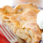 Slice of apple pie with top crust and a scoop of vanilla ice cream with a fork