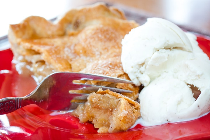 Slice of apple pie with top crust and a scoop of vanilla ice cream with a fork