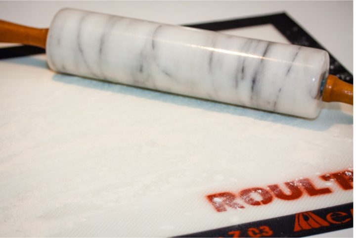 Silicone mat with flour sprinkled on it and a marble rolling pin to the side