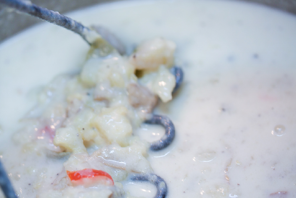 Potato masher in a bowl of baked potato soup.