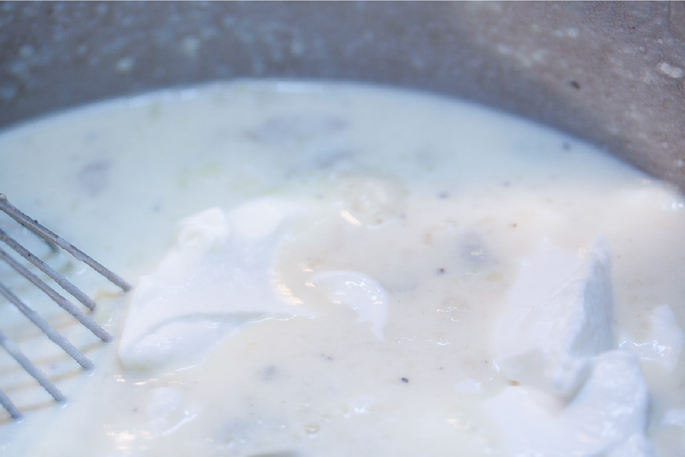 A whisk mixing sour cream into a bowl of baked potato soup.