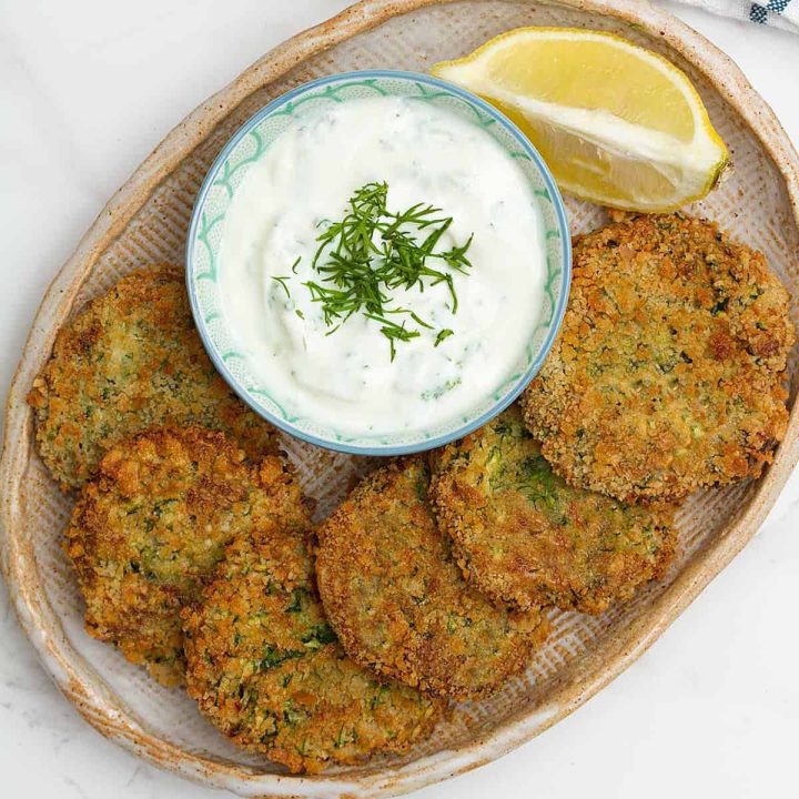 Zucchini air fryer fritters on a platter with a dish of garlic aoli.