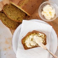 Overhead shot of a loaf of zucchini bread with a slice being spread with clotted cream and text Zucchini Sweet Bread, recipes and ideas using zucchini Menus4Moms
