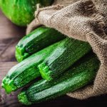 Jute bag filled with zucchini on a wooden surface