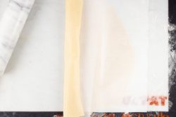 pie crust dough partially rolled up in parchment paper on a rolling mat with a marble rolling pin to the side