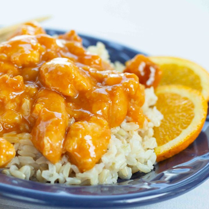 Pieces of cubed chicken in a breading with an orange sauce on a bed of rice and garnished with orange slices.