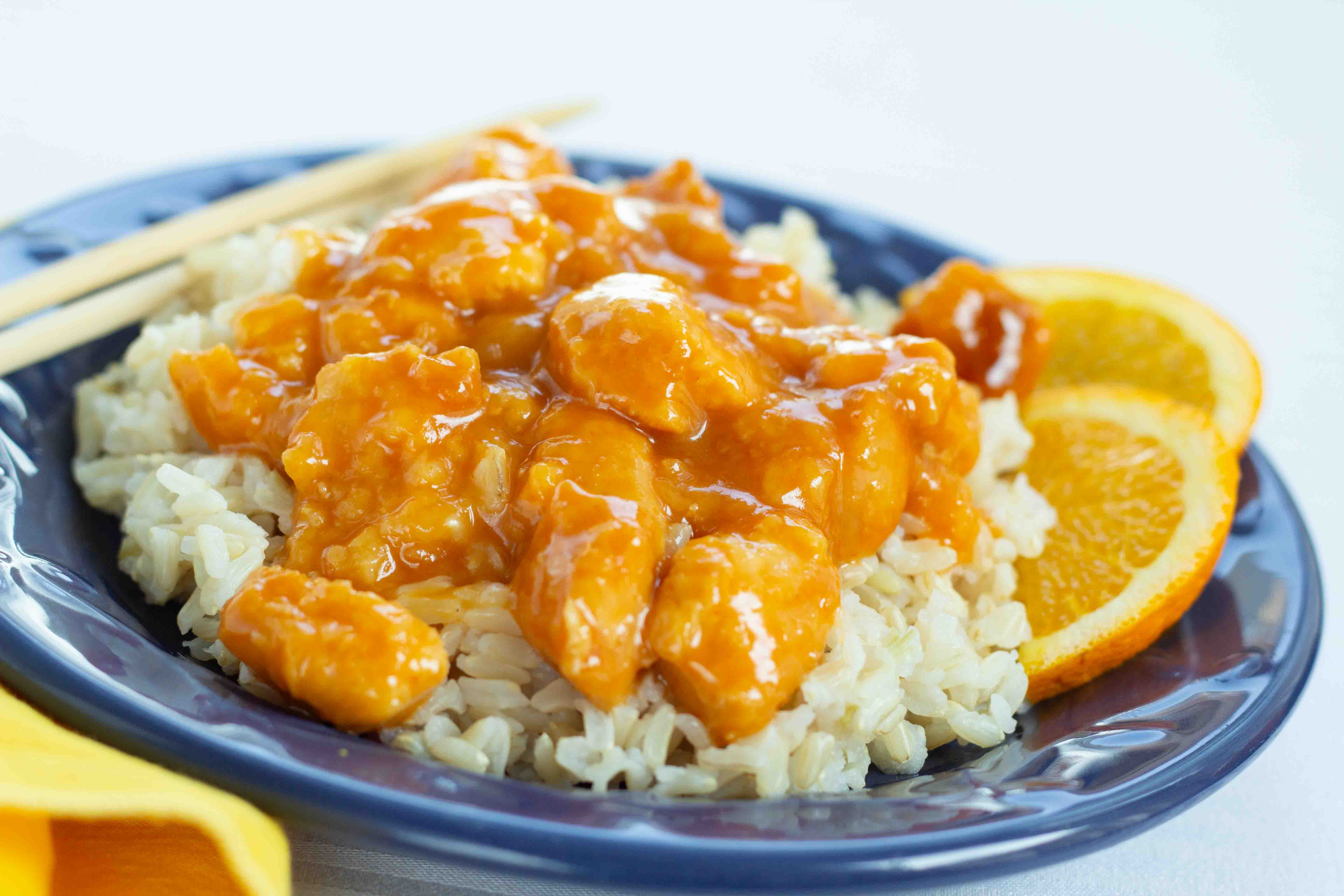 Pieces of cubed chicken in a breading with an orange sauce on a bed of rice and garnished with orange slices.