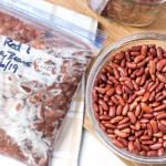 Overhead shot of bowl of dried kidney beans with a strainer and a bowl of great northern beans on a cutting board