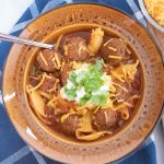 Overhead shot of albondigas soup (Mexican meatball soup) in a brown wide-rim bowl garnished with sour cream, grated cheddar cheese, and fresh cilantro