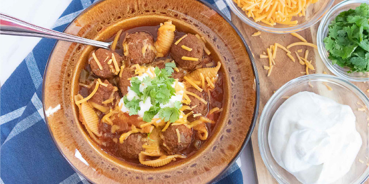 Overhead shot of albondigas soup (Mexican meatball soup) in a brown wide-rim bowl garnished with sour cream, grated cheddar cheese, and fresh cilantro