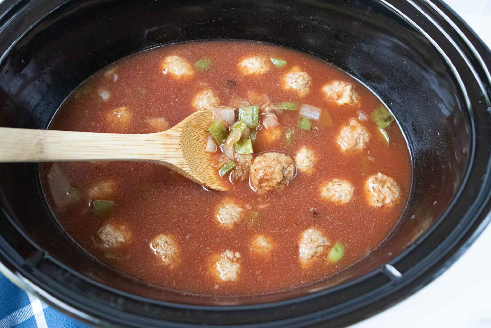 Overhead view of meatballs, onions, and bell peppers cooking in a beef and tomato broth in a crockpot