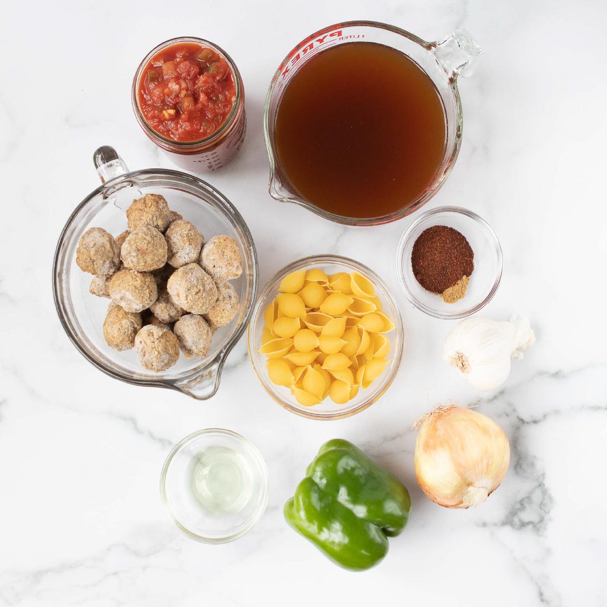Overhead shot of ingredients: meatballs, salsa, beef broth, spices, shell pasta, olive oil, garlic bulb, onion, green bell pepper