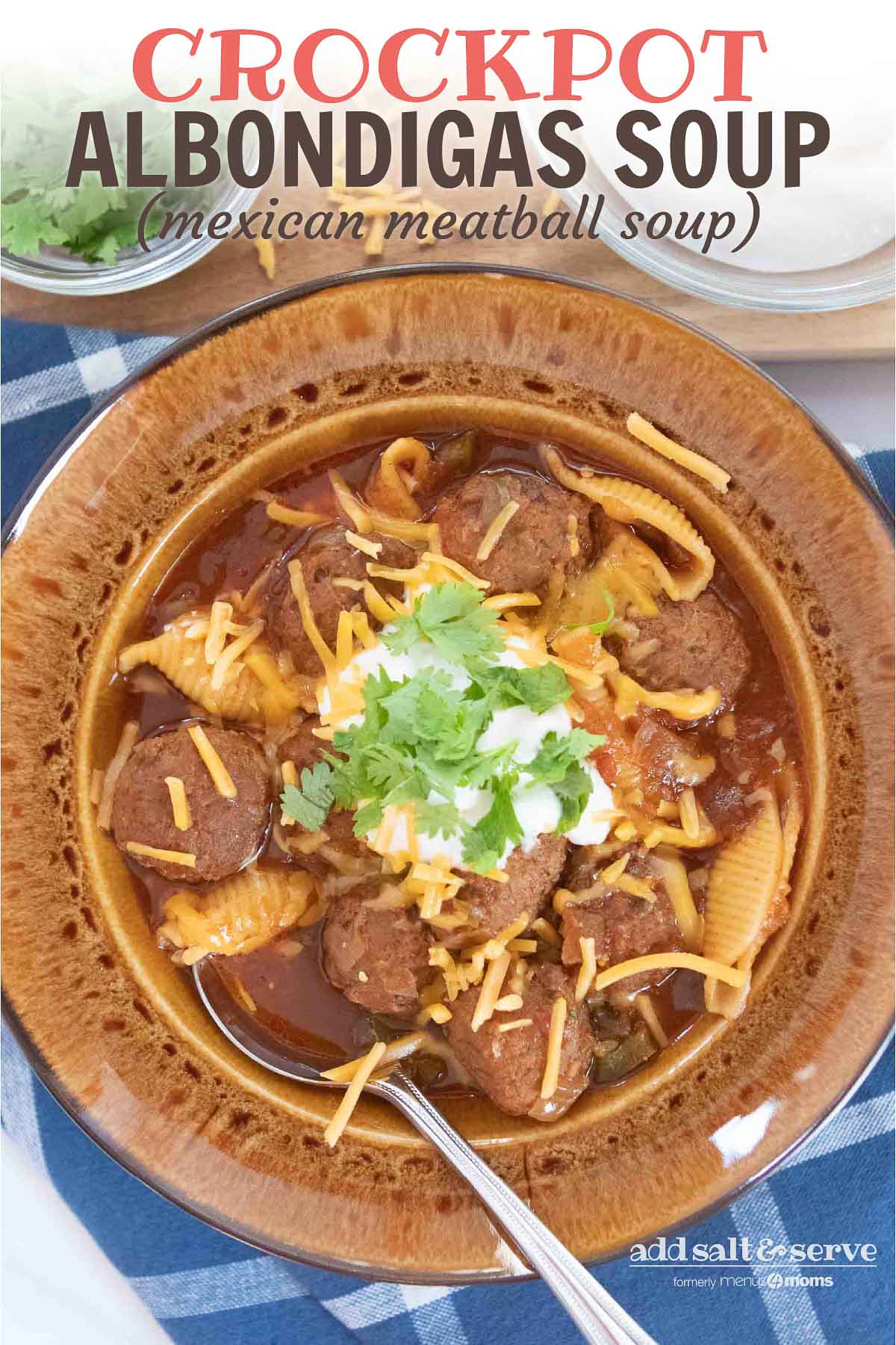Overhead shot of albondigas soup (Mexican meatball soup) in a brown wide-rim bowl garnished with sour cream, grated cheddar cheese, and fresh cilantro