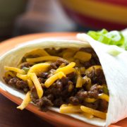 Burrito with ground beef and shredded cheddar cheese garnished with diced green onions.