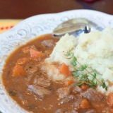 Beef and Guinness Stew over mashed potatoes in a white bowl with a spoon and a sprig of thyme