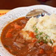 Beef and Guinness Stew over mashed potatoes in a white bowl with a spoon and a sprig of thyme