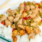 Diced chicken and diced red and green bell peppers on a bed of rice on a transparent square glass plate.