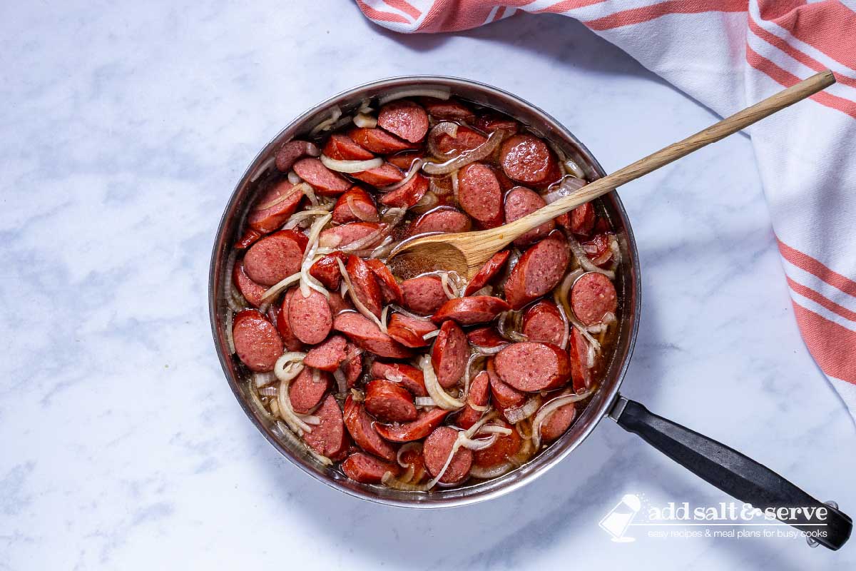 Skillet with cooked Brown Sugar Kielbasa with a wooden spoon.