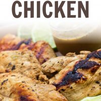 Grilled chicken on a square plate, garnished with lime slices. A small clear glass cup of Dijon basil lime dipping sauce is on the plate. Text Basil Lime Chicken add salt & serve formerly menus4moms