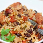 White bowl and fork with rice, black beans, sausage, tomatoes, and green chilies