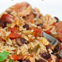White bowl and fork with rice, black beans, sausage, tomatoes, and green chilies. Text Chicken and Sausage Jambalaya Add Salt & Serve formerly Menus4Moms