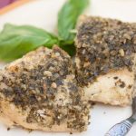 Two bite-size pieces of chicken topped with pesto beside a fork, on a white plate