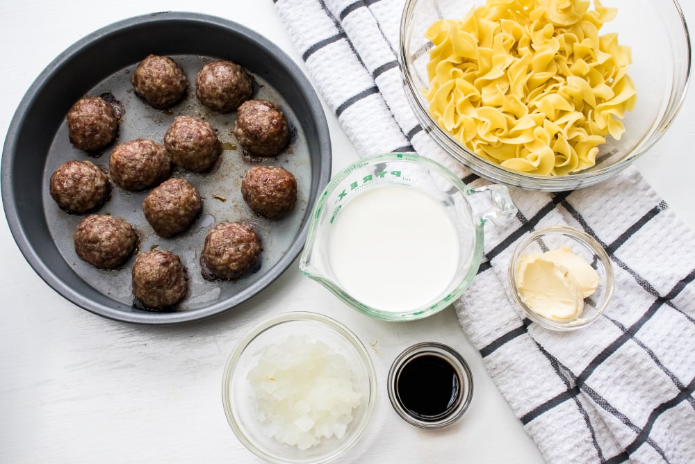 Meatballs in a pan and bowls of ingredients: cooked egg noodles, cream, chopped onion, balsamic vinegar, and butter