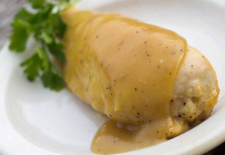 White plate with chicken breast topped with a Dijon sauce.