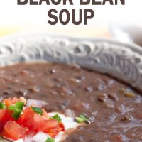 A white shallow bowl with Black Bean Soup garnished with sour cream, diced tomatoes, diced red onion, and fresh cilantro and text Black Bean Soup add salt & serve formerly Menus4Moms