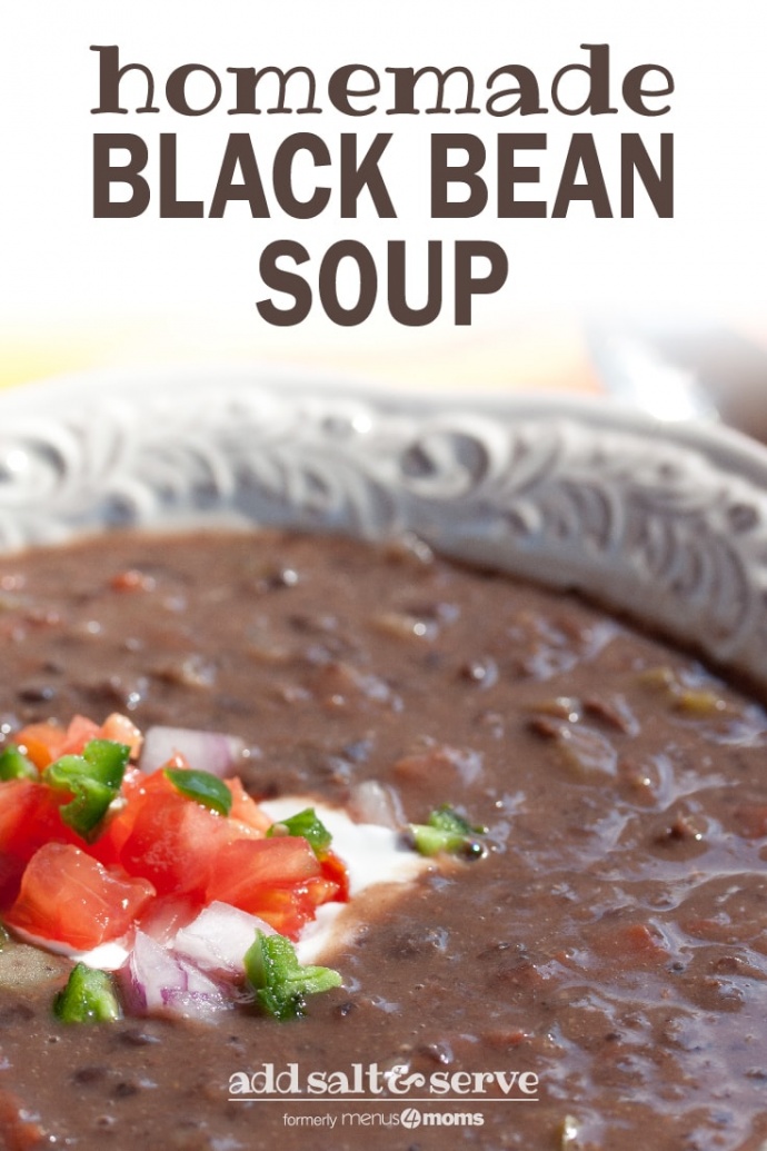 A white shallow bowl with Black Bean Soup garnished with sour cream, diced tomatoes, diced red onion, and fresh cilantro and text Black Bean Soup add salt & serve formerly Menus4Moms