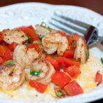 Shrimp, diced tomatoes, and shredded cheddar cheese on grits, on a white plate with a fork.