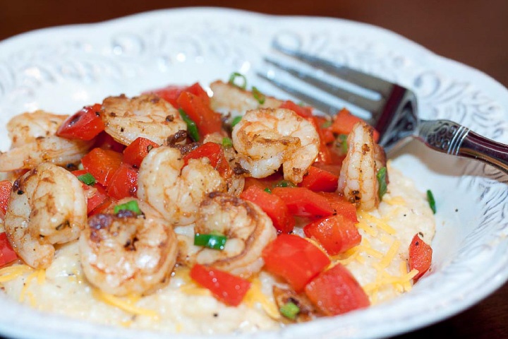 Shrimp, diced tomatoes, and shredded cheddar cheese on grits, on a white plate with a fork.