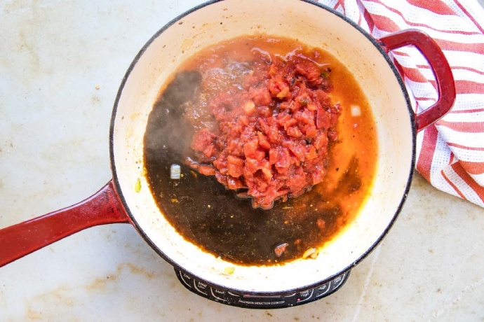Worcestershire sauce and diced tomatoes in a red and white skillet. There is a red and white striped dish towel beside the skillet.