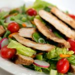 Salad of romaine lettuce pieces, grape tomatoes, and carrots topped with sliced grilled chicken