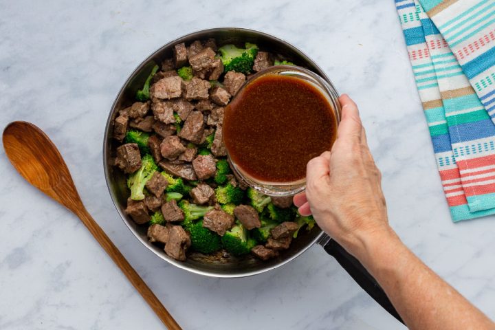 pouring sauce over leftover steak and broccoli in a skillet
