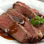 Four slices of sliced roast beef on a white plate with brown gravy on top. Garnished with a sprig of parsley