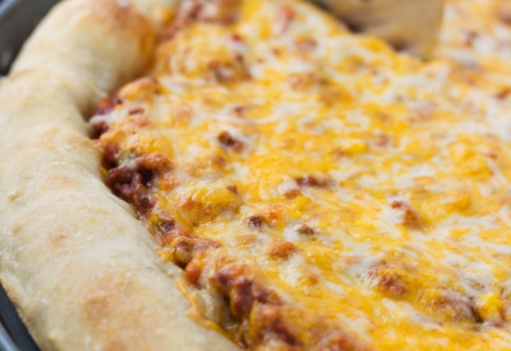 Side view of a whole pizza with sloppy joe sauce covered with colby-jack cheese on a thick crust