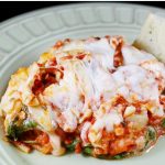 Lasagna with spinach, tomato sauce, and melted mozzarella cheese on a plate with a slice of italian bread