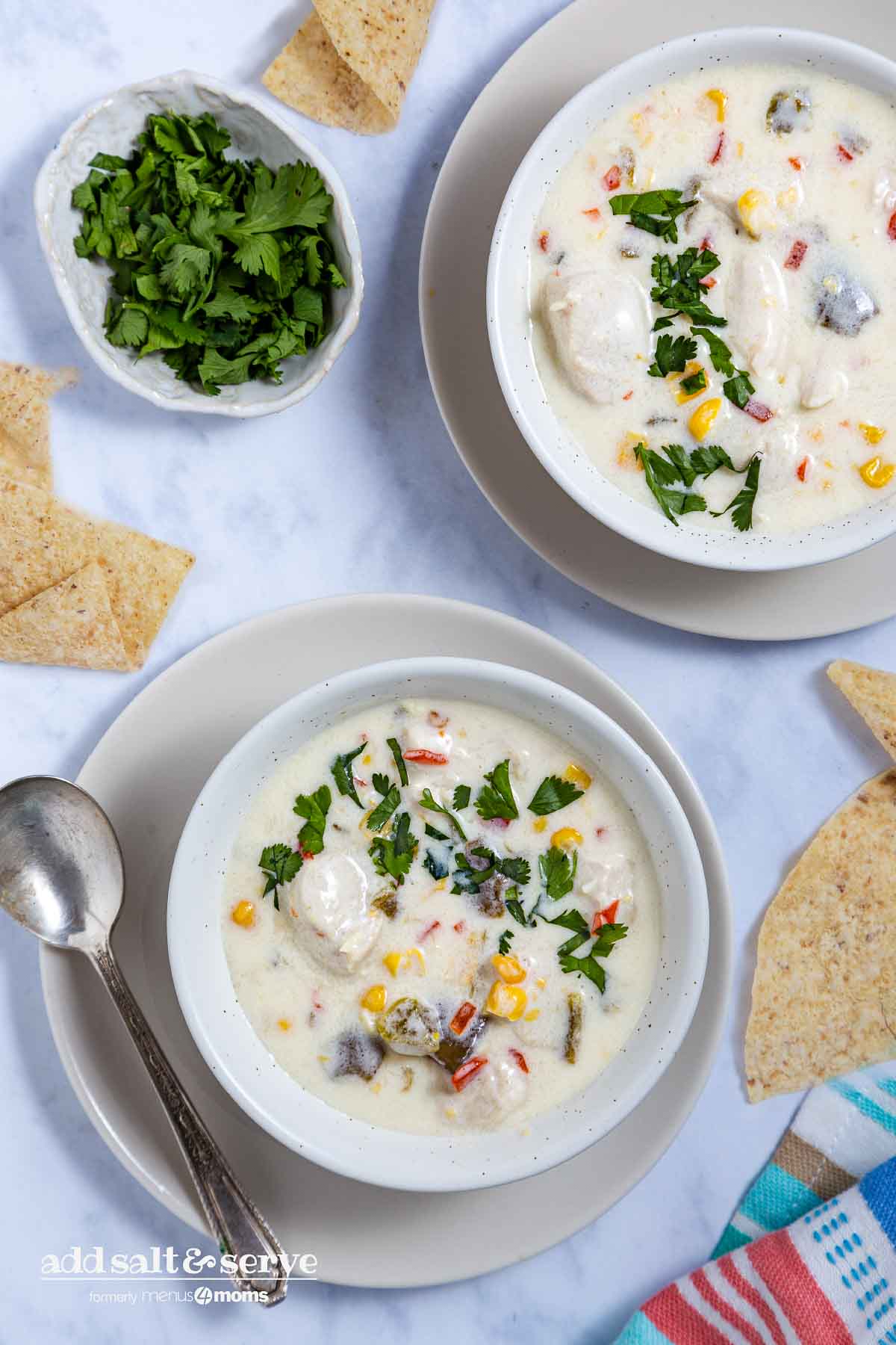 Tex-Mex Chicken Corn Chowder Recipe Two bowls of Southwest Chicken Corn Chowder on saucers with cilantro and tortilla chips to the side.