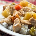 Chunks of cooked chicken, pinapple, carrots, and peppers served over white rice